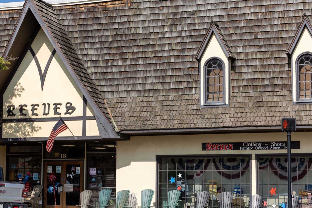 5Y8A8465A - Reeves 1928 Front of Reeves clothing store with a Tudor-style gable, American flag, and patriotic window displays outside the entrance.