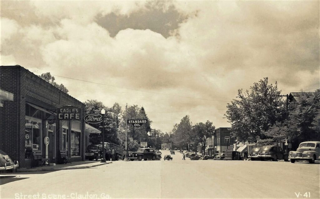 Vintage street scene with brick storefronts, Eagle's Cafe sign, Ford and Standard Oil signs, and 1950s cars along the curb.
