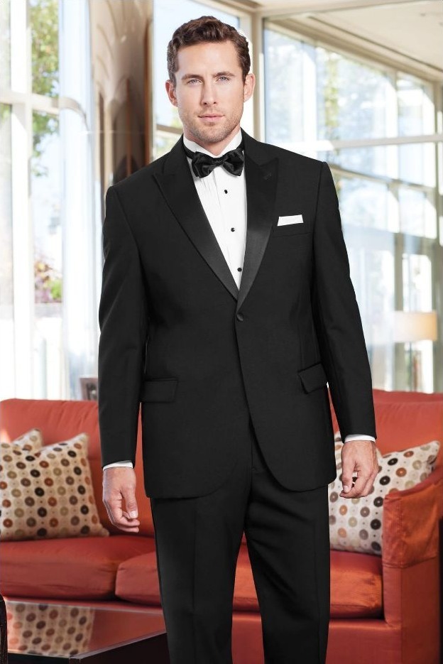 Reeves Tuxedo Rental (Black Classic Peak Tuxedo) - Reeves 1928 Man in a black tuxedo with a bow tie standing indoors, looks directly at the camera.