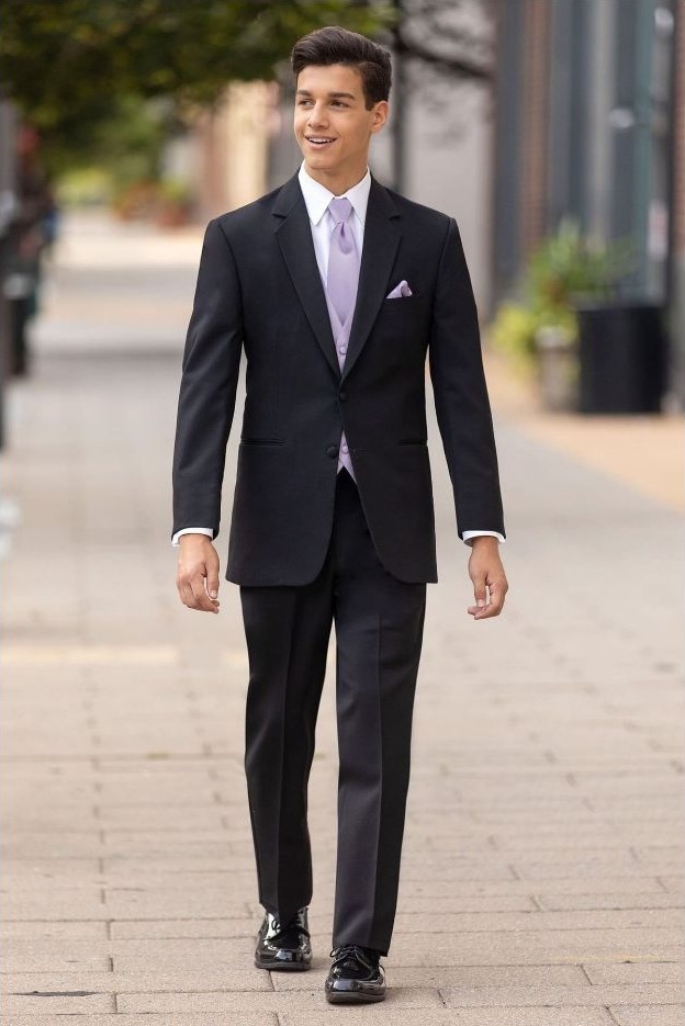 Reeves Tuxedo Rental (Black Emerson Tuxedo) - Reeves 1928 Man in a black suit walking outdoors on a sidewalk, wearing a lavender tie and pocket square.