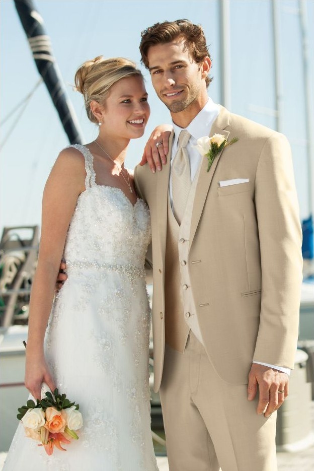 Reeves Tuxedo Rental (Tan Havana Suit) - Reeves 1928 Bride in a white lace wedding gown and groom in a tan suit pose together by a marina, holding a bouquet.