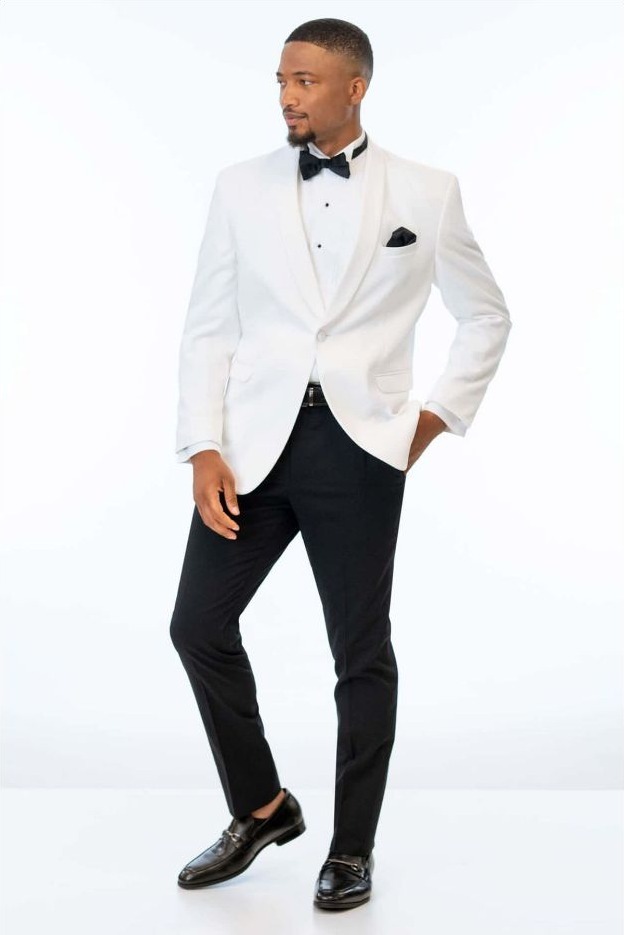 Reeves Tuxedo Rental (White Classic Dinner Jacket Tuxedo) - Reeves 1928 Man wearing a white tuxedo jacket with a black bow tie, black trousers, and dress shoes, posing with one hand in pocket.