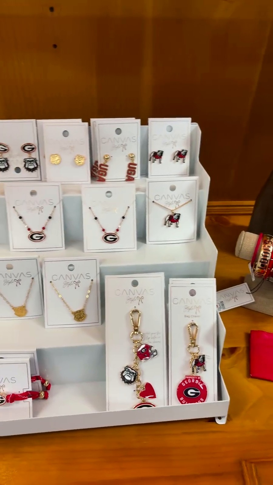 Assorted CANVAS jewelry display on white stand featuring necklaces and earrings with Georgia Bulldogs logos and mascots.