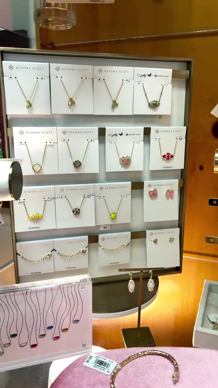 Display of multiple Kendra Scott necklaces on white cards arranged in a jewelry case.