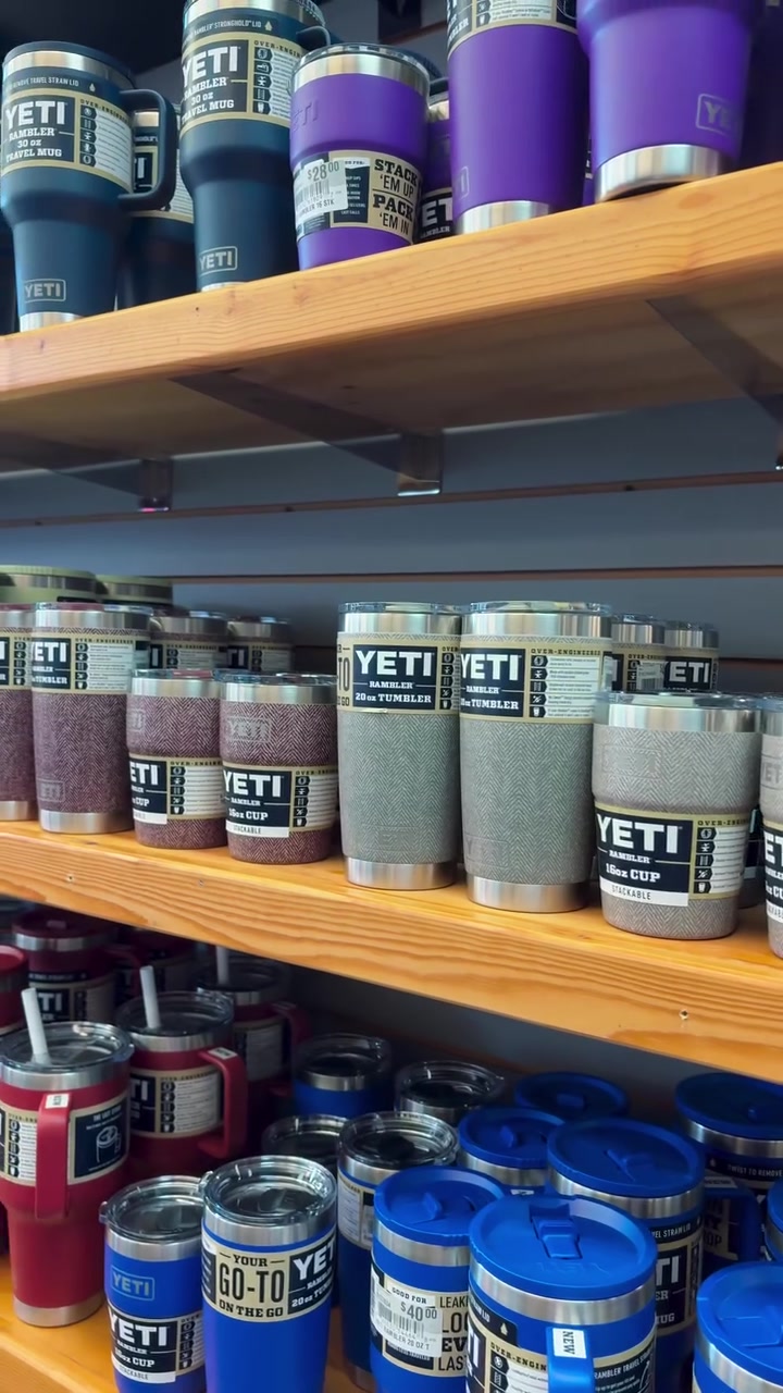 Shelves display a row of YETI Rambler tumblers in blue, purple, and gray with label wraps on a wooden shelf, various sizes visible.